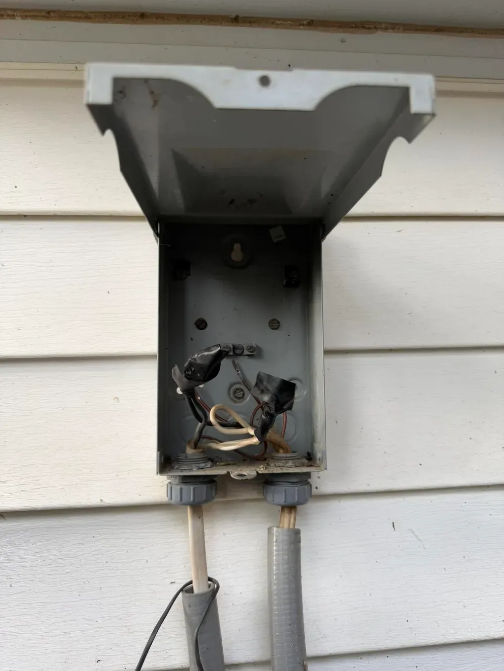 An open electrical disconnect box mounted on the siding beside a Simpsonville condenser