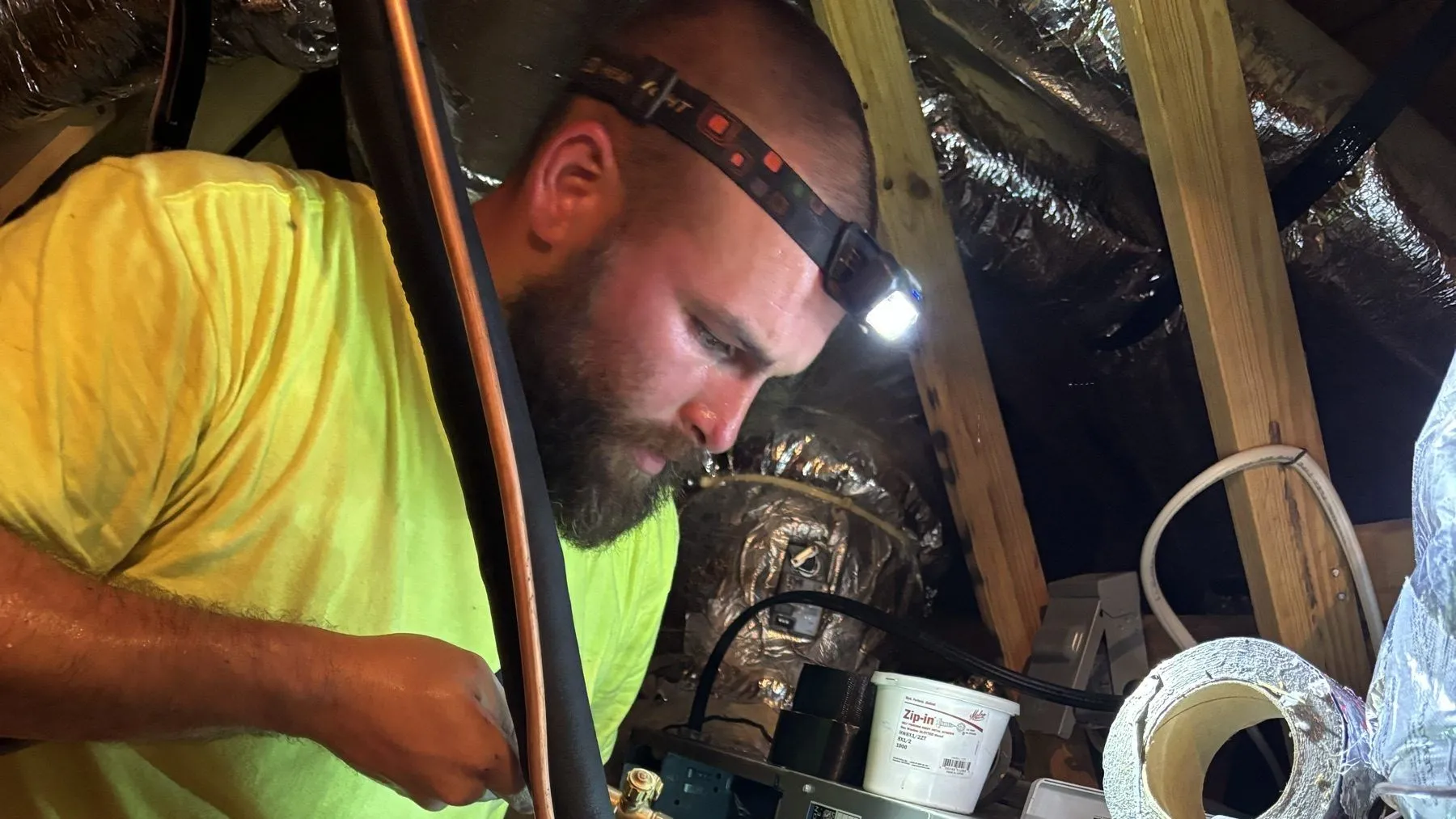 Rhino HVAC technician brazing a copper line set by headlamp in an attic