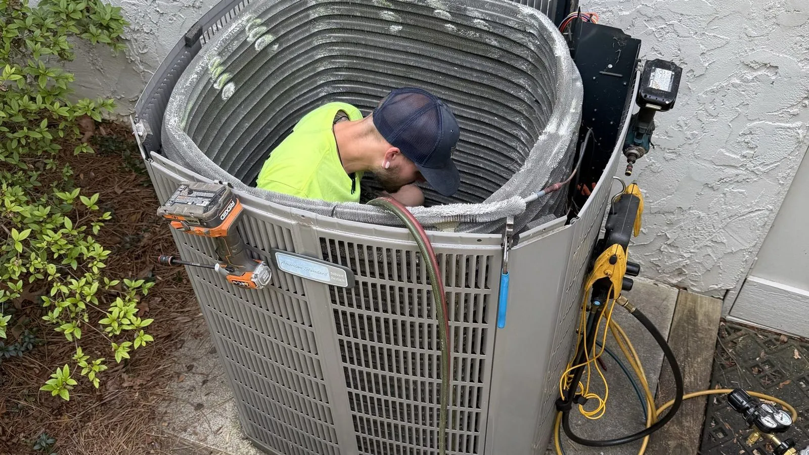 A Rhino HVAC technician leaning inside an opened outdoor unit to clean the condenser coil