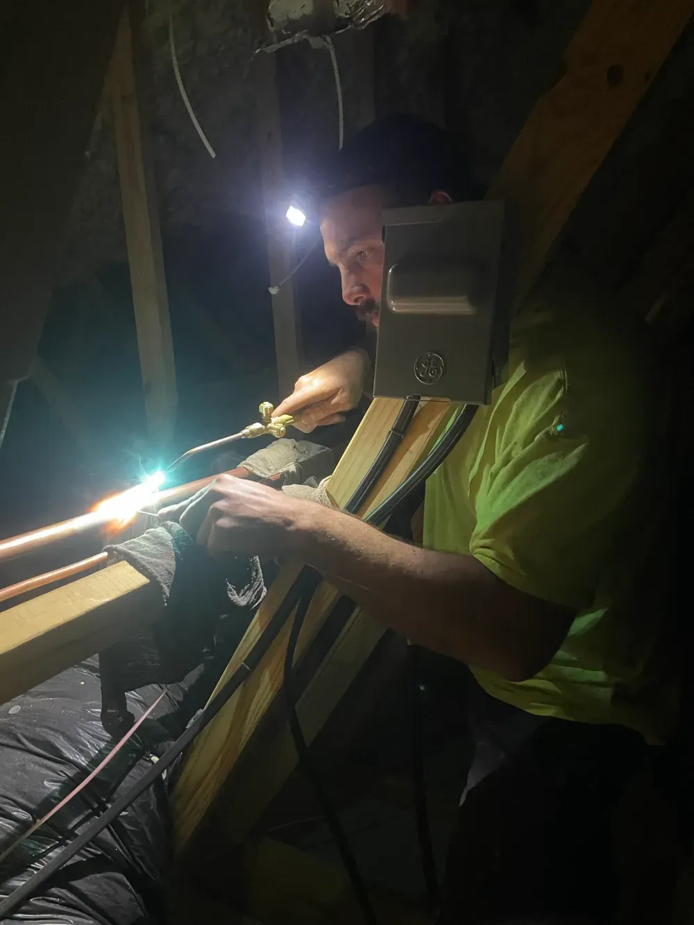 A Rhino HVAC technician brazing a copper line set in a Simpsonville attic