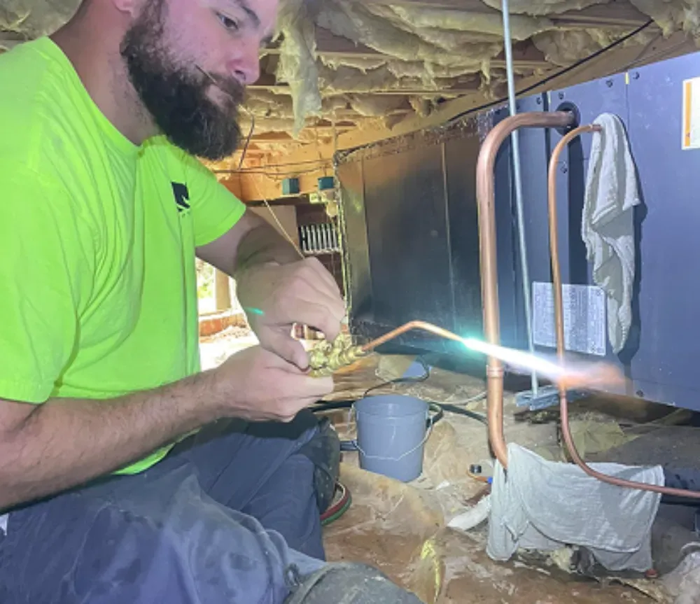 A Rhino HVAC technician brazing copper pipes over a bucket in Greer