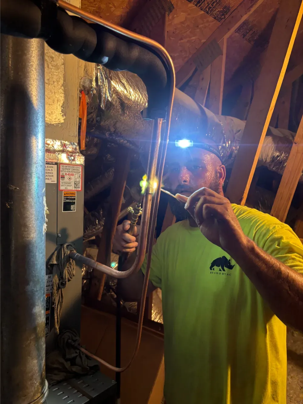 A Rhino HVAC technician brazing a line set beside ductwork in Greenville