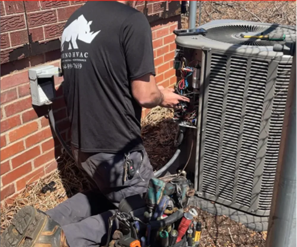 A Rhino HVAC technician repairing a condenser panel with an open tool bag beside him in Greer
