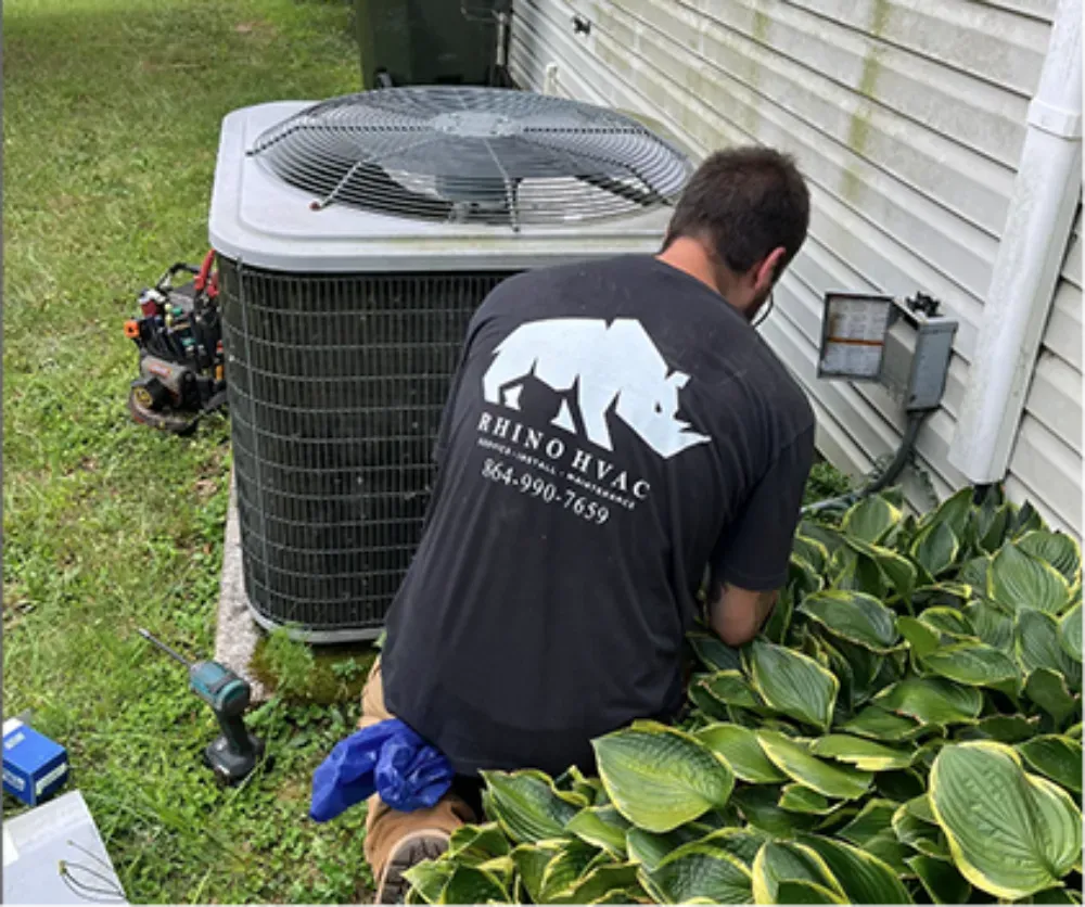 A Rhino HVAC technician servicing a condenser beside a bed of hostas at a Mauldin home