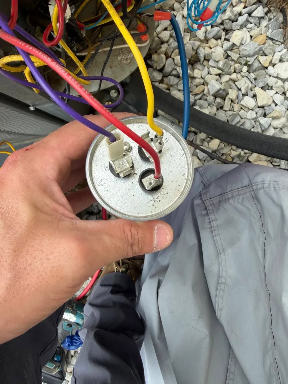 A Rhino HVAC technician holding a dual run capacitor beside an open condenser in Simpsonville