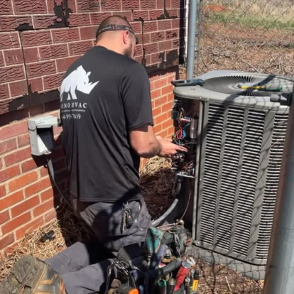 A Rhino HVAC technician servicing the open panel of an outdoor condenser in Simpsonville