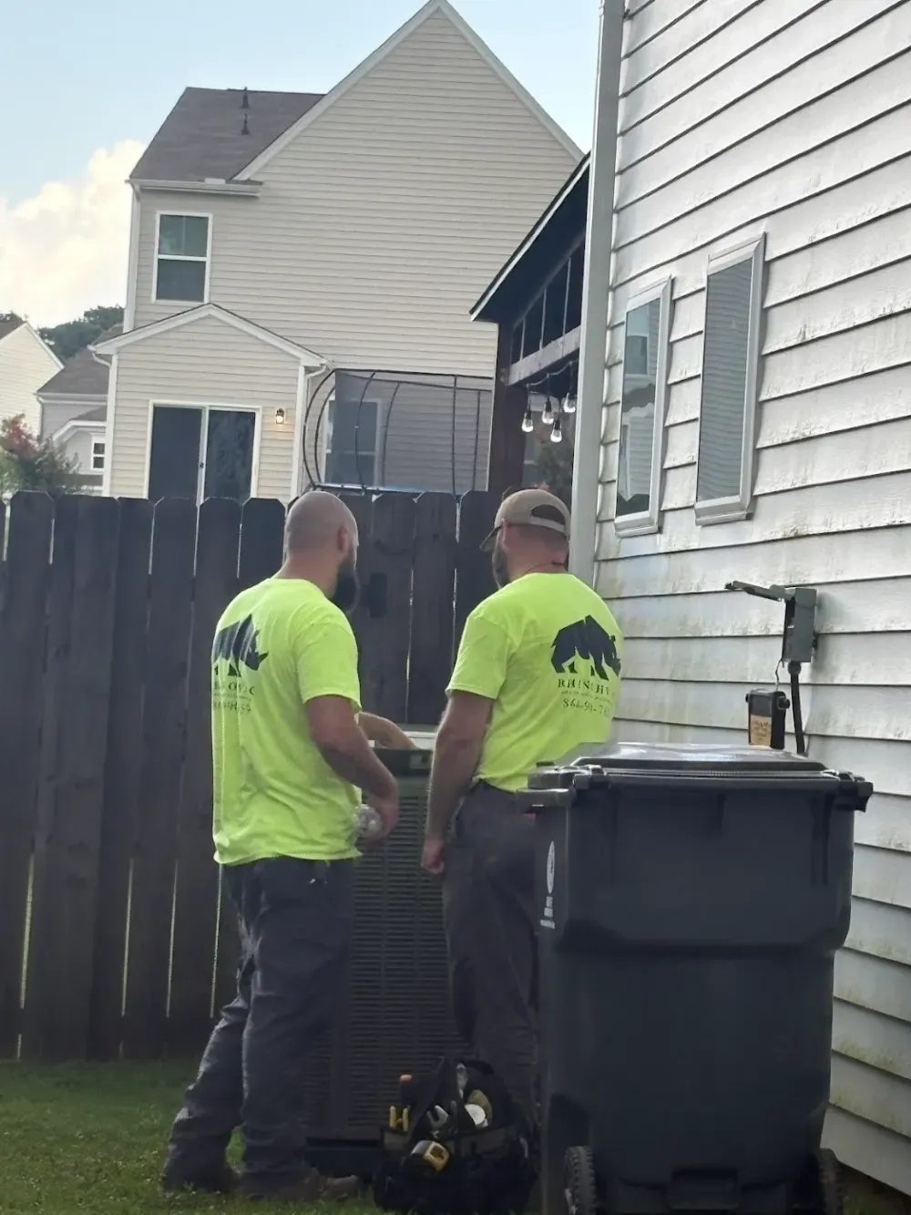 Two Rhino HVAC technicians beside a condenser near a fence at a Belton home